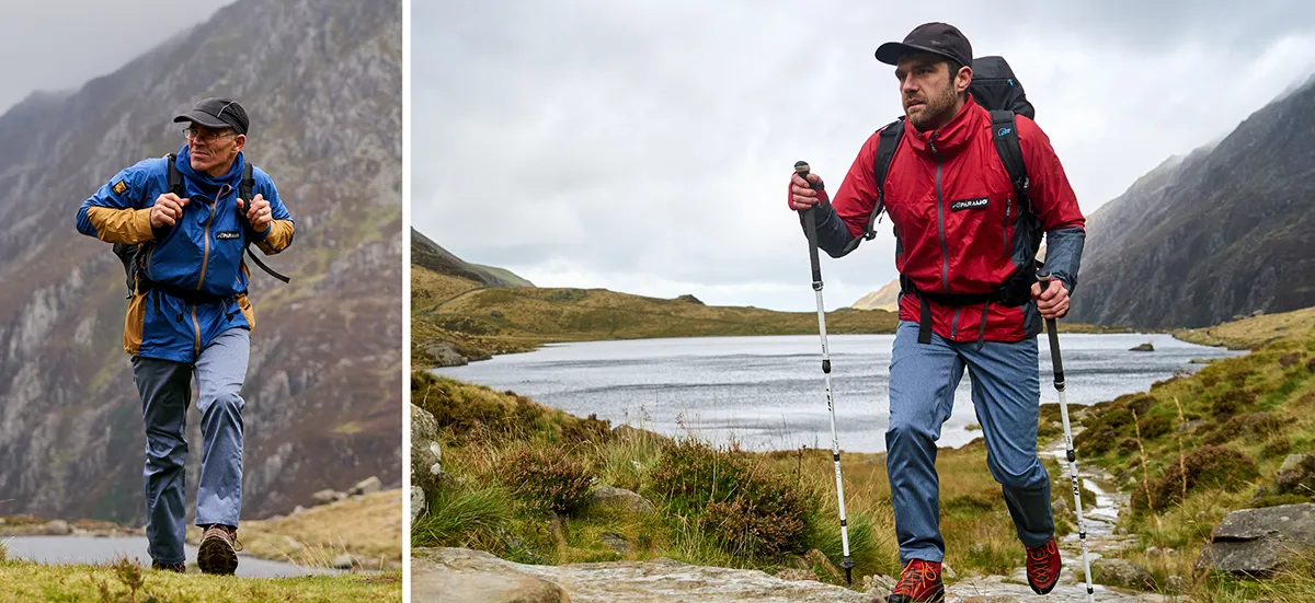 Man in windproof and backpack hiking in the rain with walking sticks past a lake