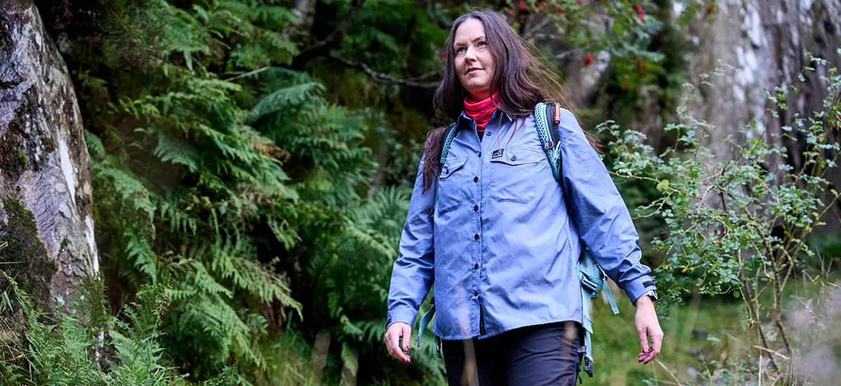 Woman wearing blue outdoors shirts with a backpack hiking near a rock